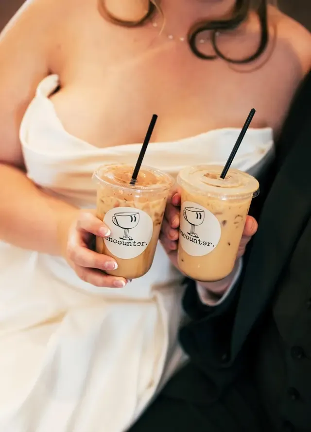 Two iced coffees in Encounter Coffee branded cups held by a bride