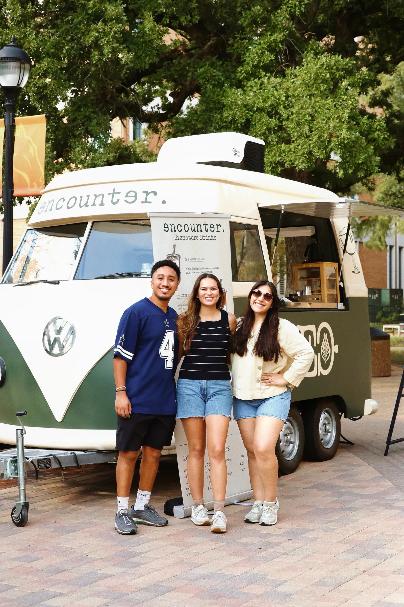 The Encounter Coffee team standing in front of their VW bus coffee trailer at an outdoor Dallas–Fort Worth event